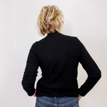 Person wearing a black ribbed sweater and blue jeans against a white background