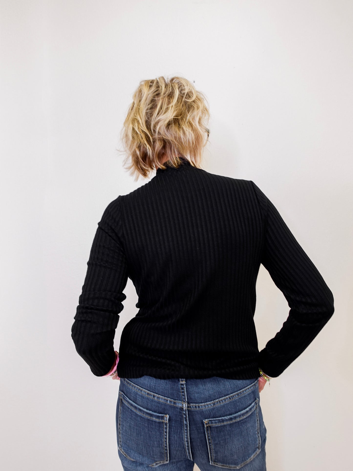 Person wearing a black ribbed sweater and blue jeans against a white background