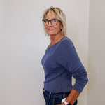 Woman wearing a blue sweater and glasses against a white wall