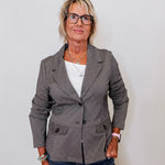 Woman wearing a camel blazer over a white shirt with a plain background