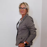 Woman wearing a brown blazer and glasses against a plain background