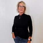 Person wearing a black ribbed sweater and blue jeans against a white wall