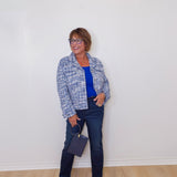 Woman standing against a white wall wearing a blue plaid jacket, blue shirt, and jeans.
