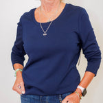 Person wearing a navy blue sweater and jeans against a plain background