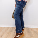 Person wearing blue jeans and brown shoes against a white wall.