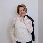 Woman wearing a white lace top and dark pants against a plain background