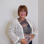 Woman wearing a white lace cardigan over a patterned top against a plain background