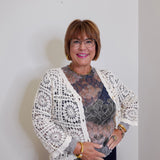 Woman wearing a white lace cardigan over a patterned top against a plain background