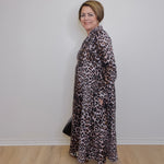 Woman wearing a leopard print dress with Adidas shoes against a white wall.