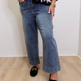 Person wearing a black and white patterned sweater, blue jeans, and black slippers on a light wooden floor.