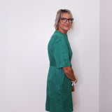 Woman wearing a green dress standing against a white wall.