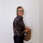 Person wearing a leopard print shirt and holding a brown bag against a white wall
