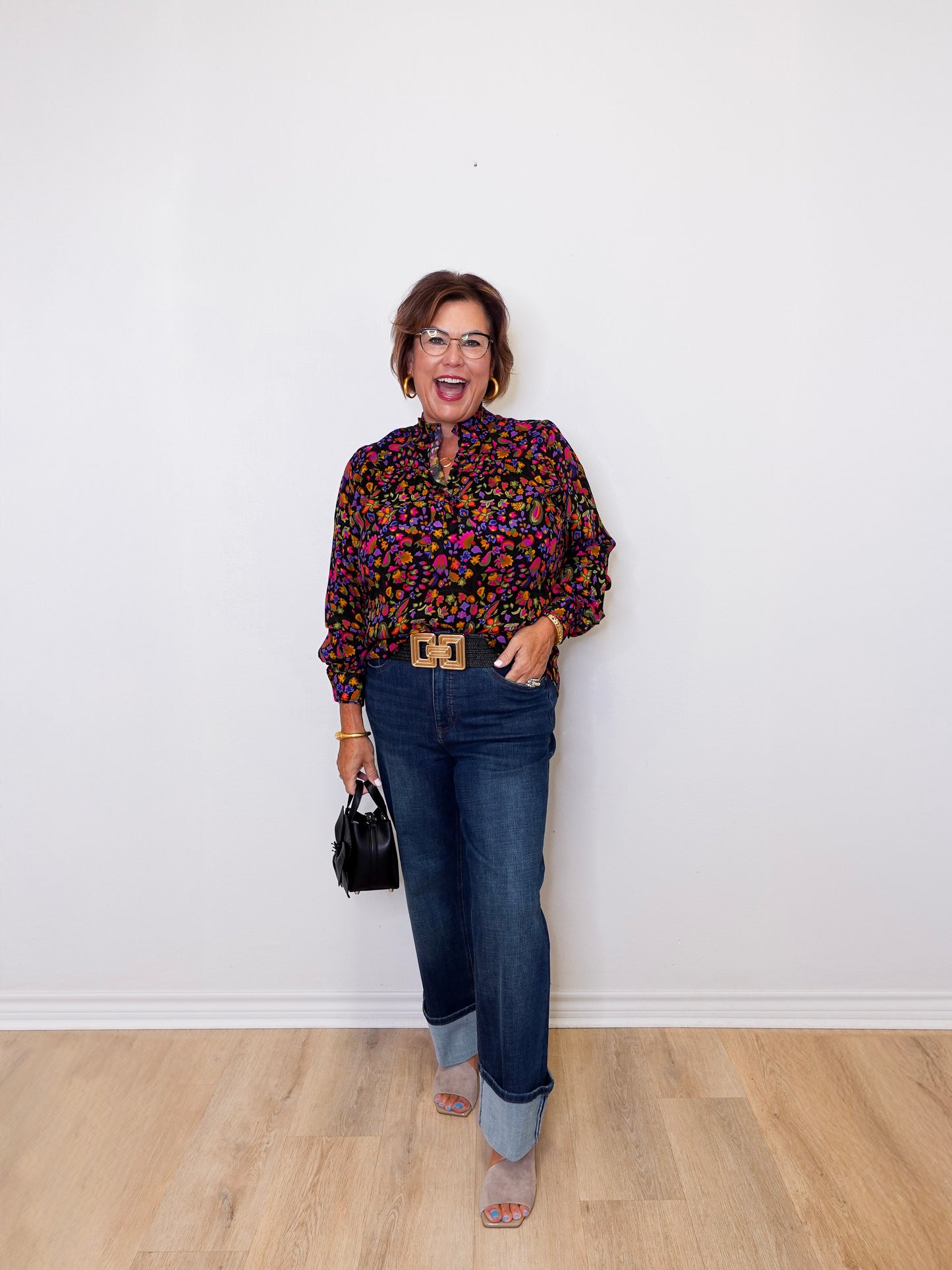 Woman wearing a colorful blouse and blue jeans against a white wall.