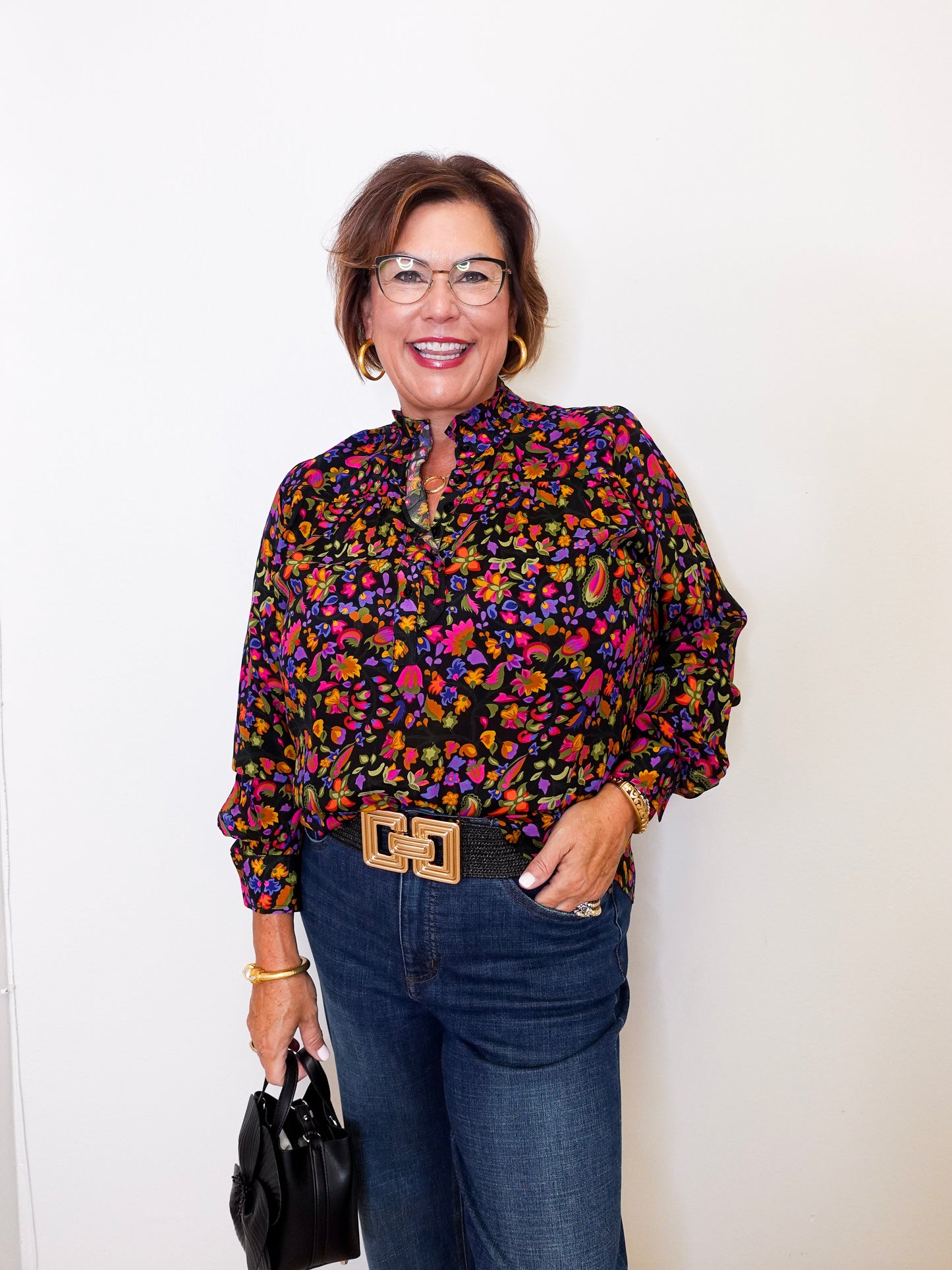 Woman wearing a colorful patterned blouse and jeans against a white background