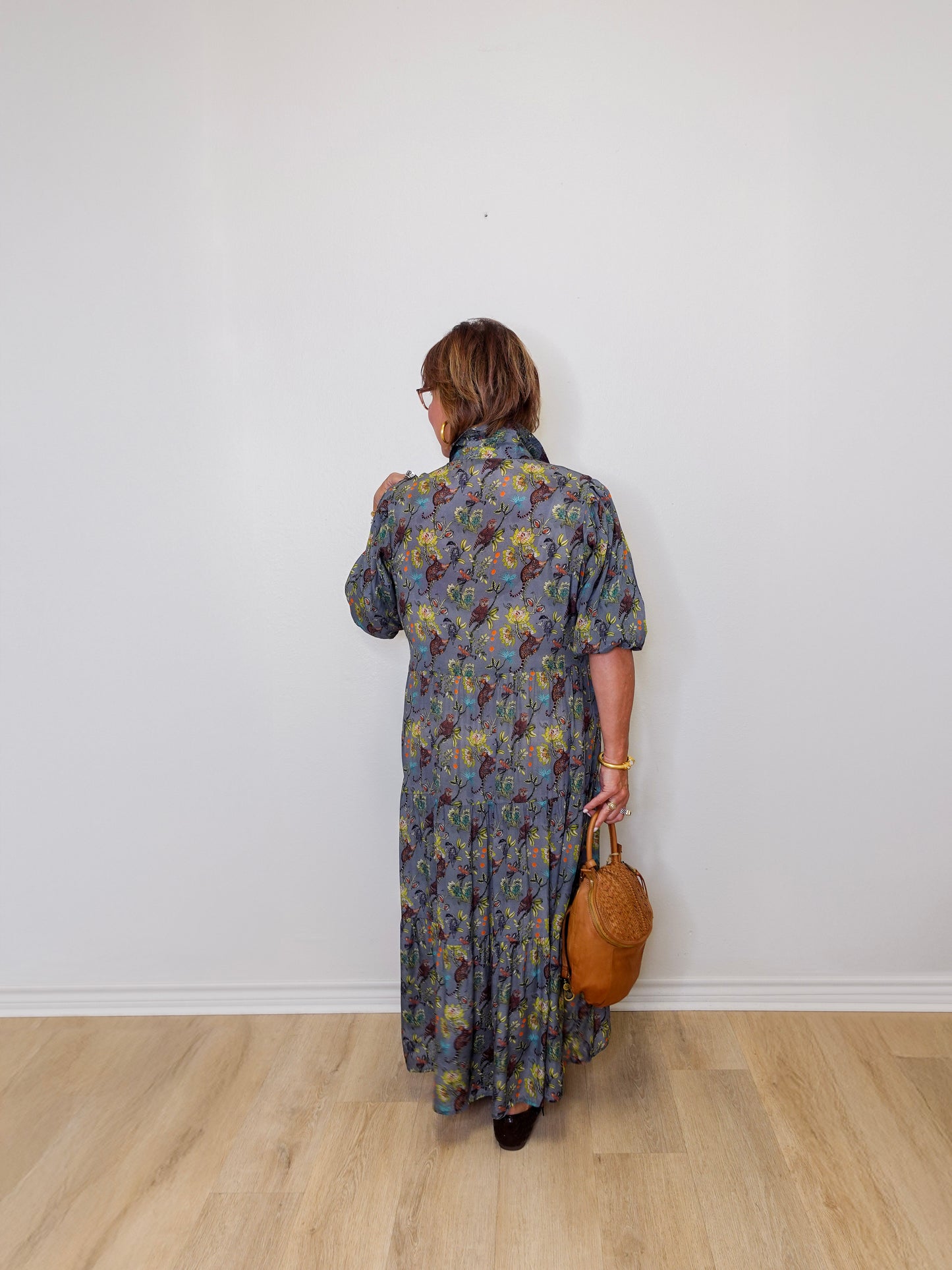 Person wearing a floral dress holding a brown bag against a white wall.