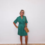 Woman wearing a green dress standing against a white wall.