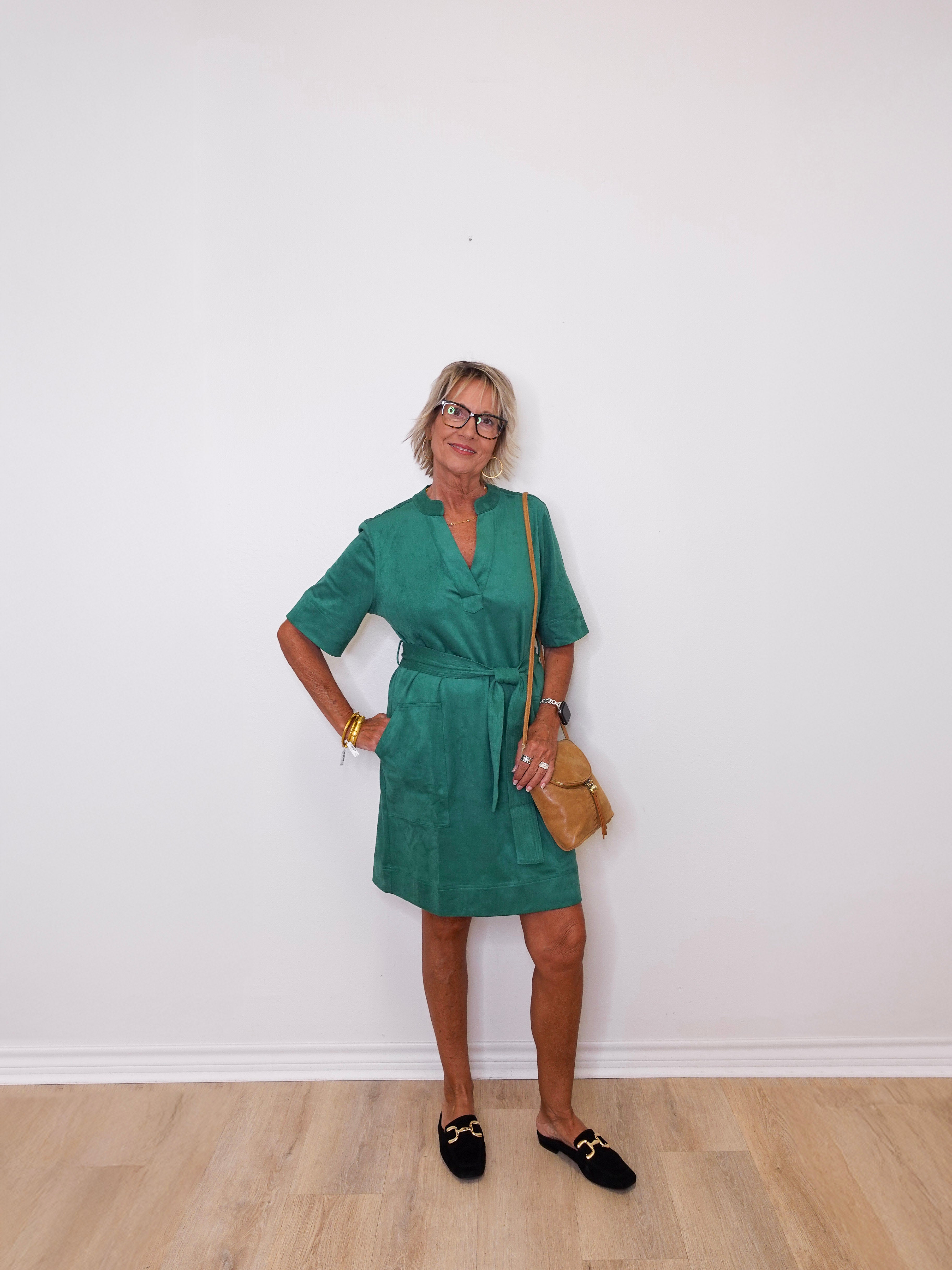 Woman wearing a green dress standing against a white wall.
