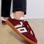 Maroon sneakers with white accents worn indoors on a wooden floor.