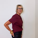Person wearing a burgundy shirt and black pants against a white wall
