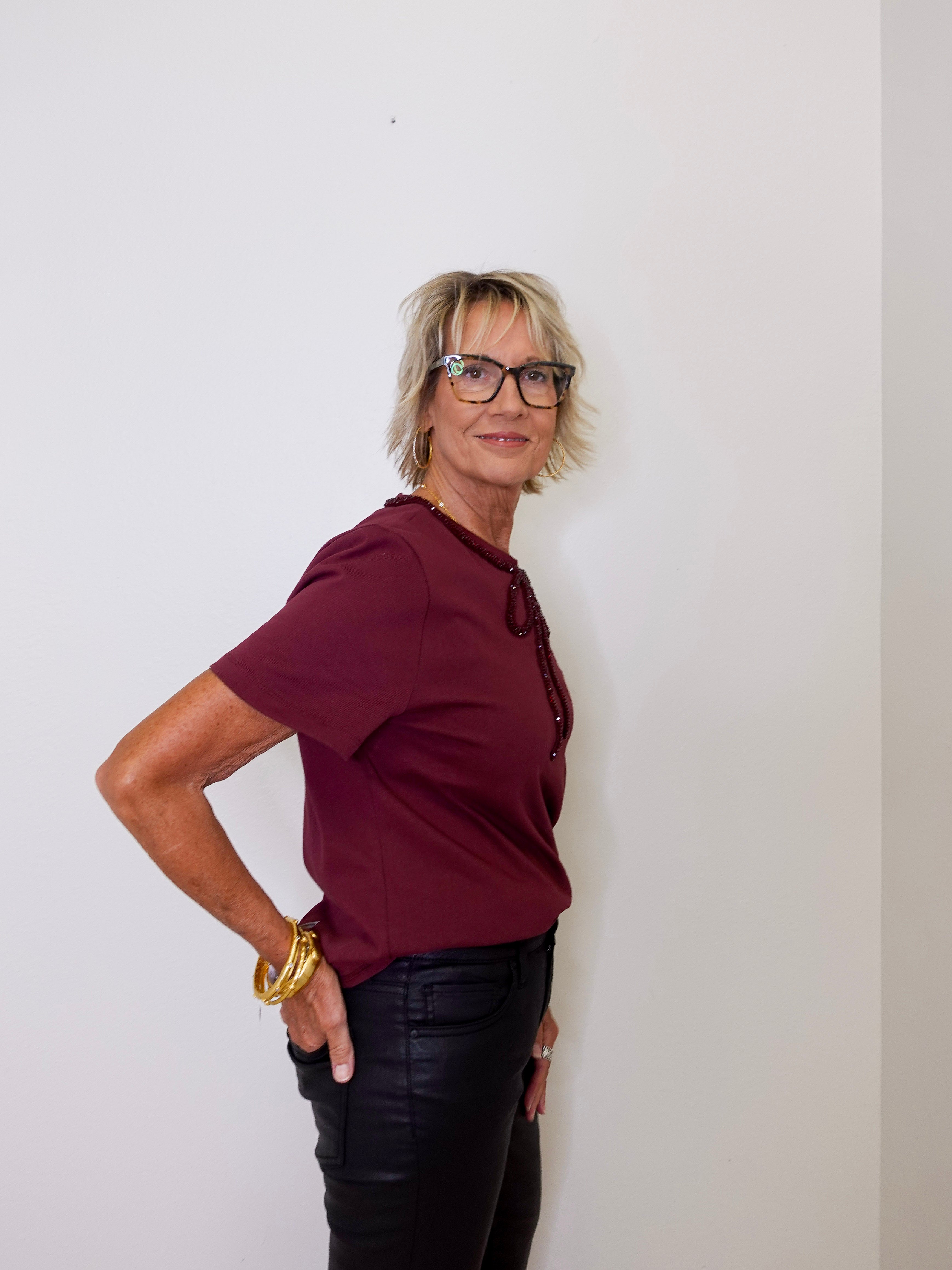 Person wearing a burgundy shirt and black pants against a white wall