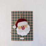 Decorative wall hanging with a beaded Santa Claus face on a plaid background
