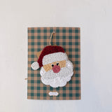 Decorative wall hanging with a beaded Santa Claus face on a plaid background