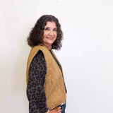 Woman wearing a beige quilted jacket over a leopard print shirt against a white background
