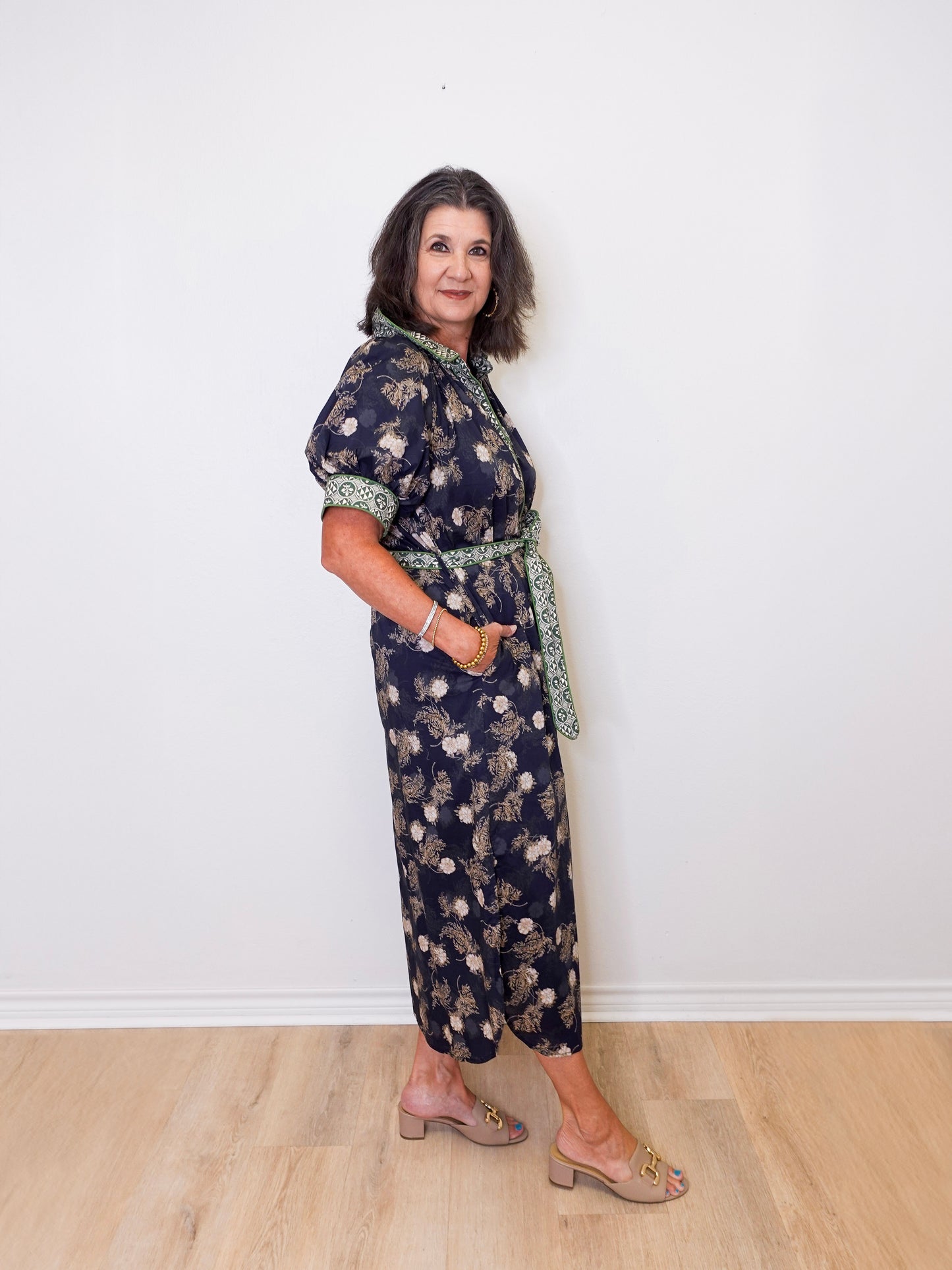 Woman wearing a floral dress standing against a white wall.