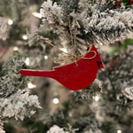 Red cardinal ornament on a snow-covered Christmas tree with blurred lights in the background