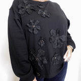Black sweater with floral embellishments worn by a person on a white background