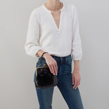 Person wearing a white sweater and blue jeans holding a black handbag against a gray background