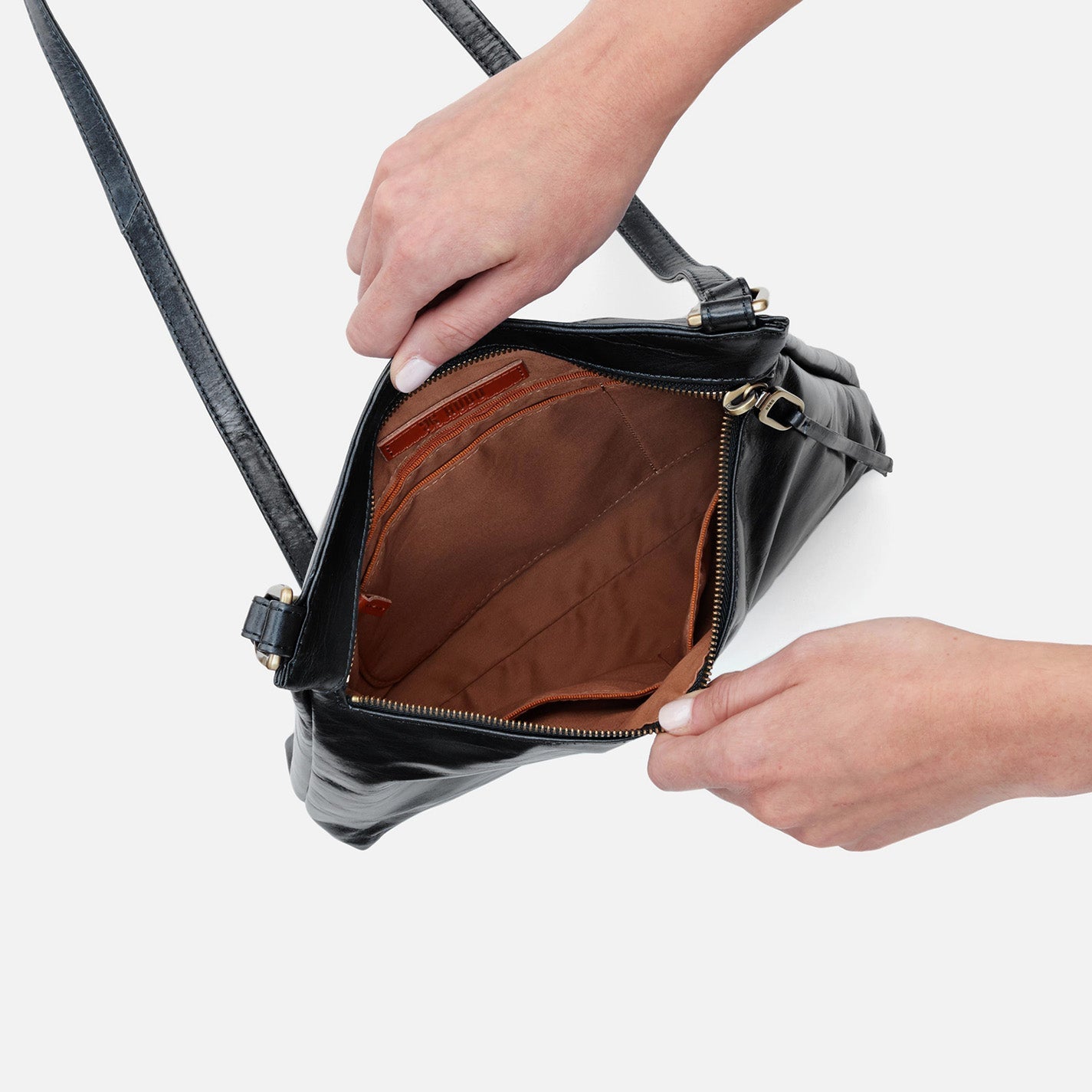 Person opening a black leather handbag with a white background