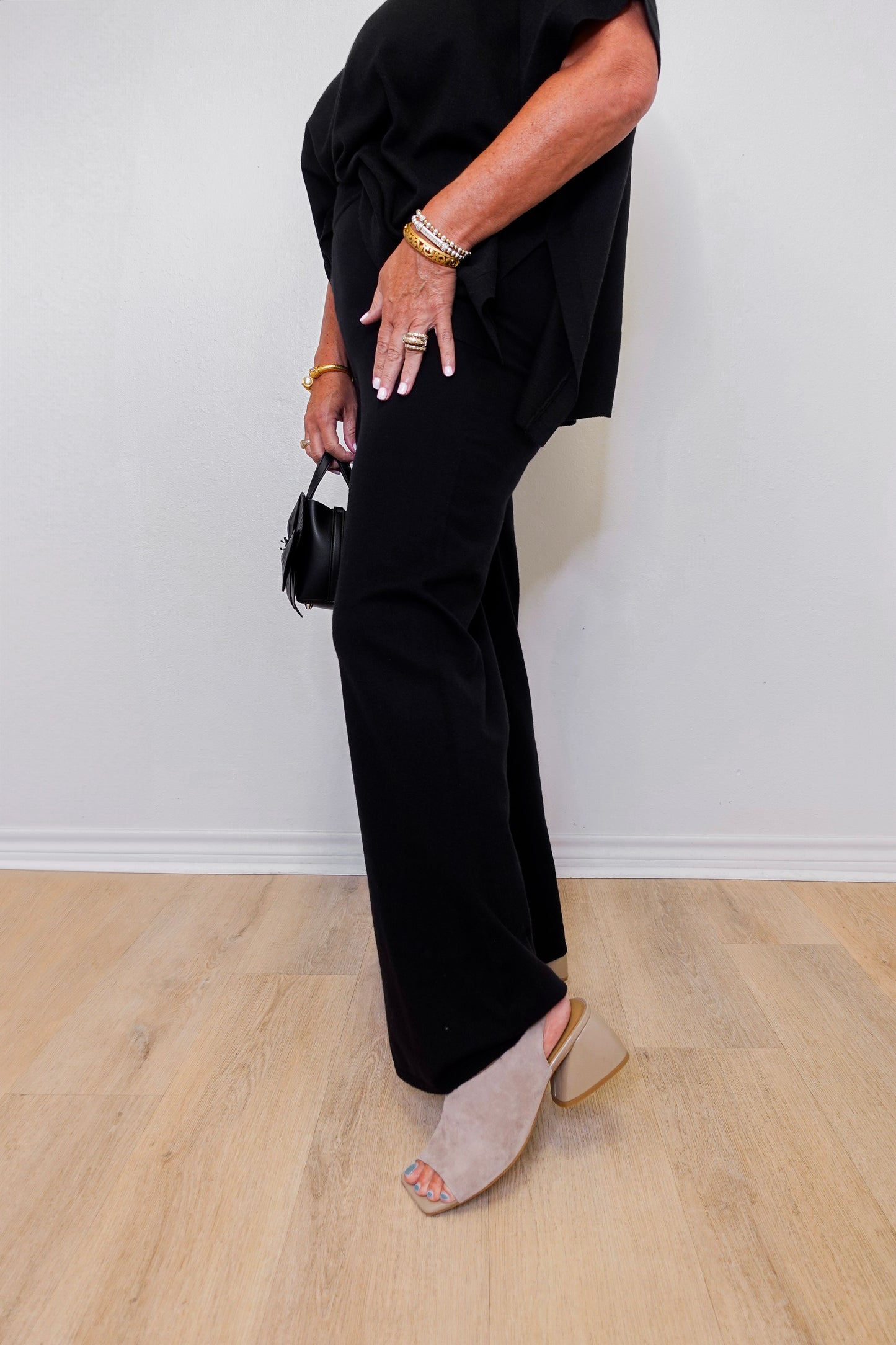 Person wearing a black outfit with wide-leg pants and open-toe shoes on a light wood floor.