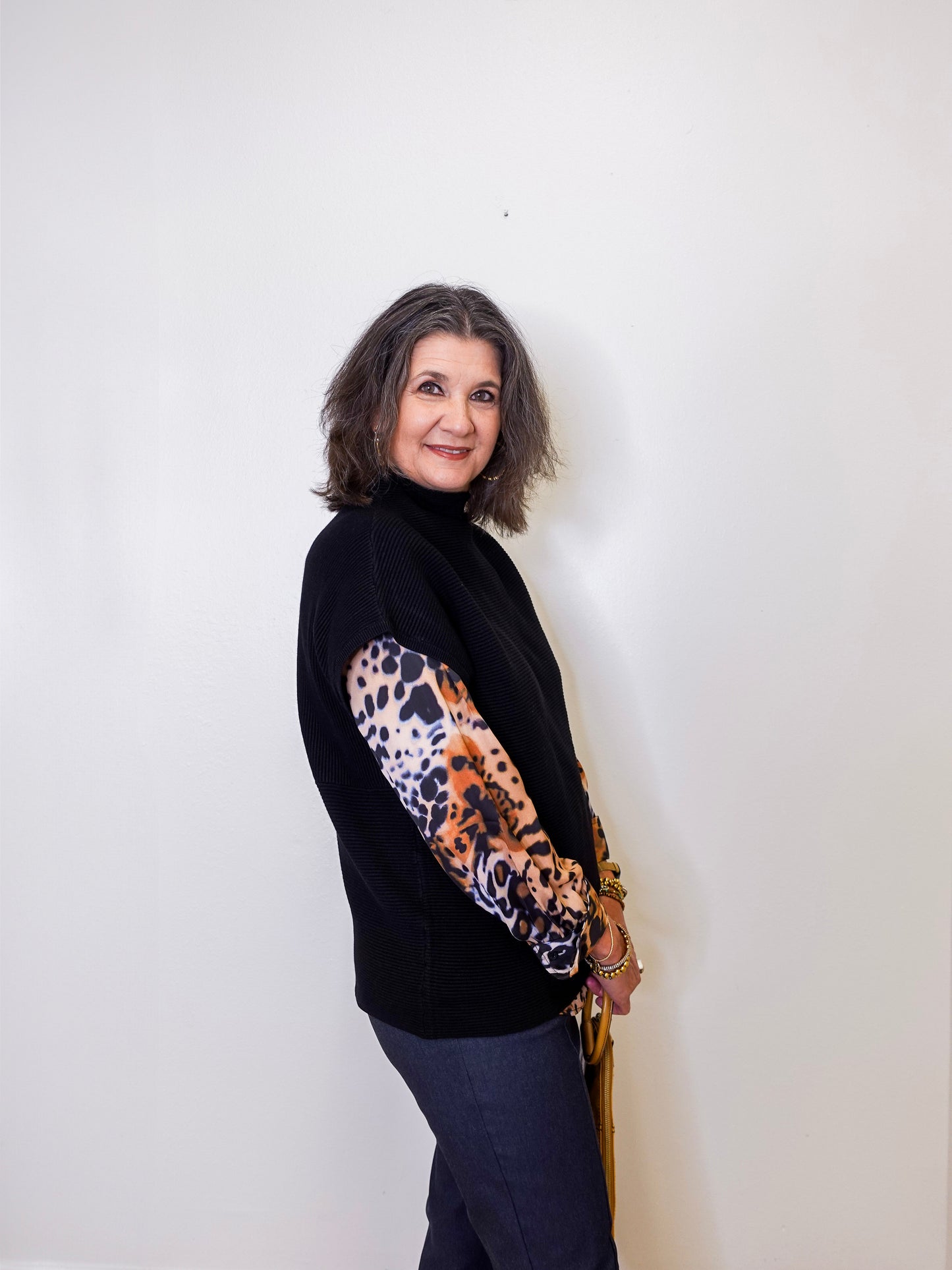 Woman wearing a black sweater with a leopard print sleeve against a white background