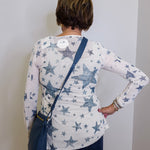 Person wearing a white long-sleeve shirt with blue star pattern, standing against a plain wall.