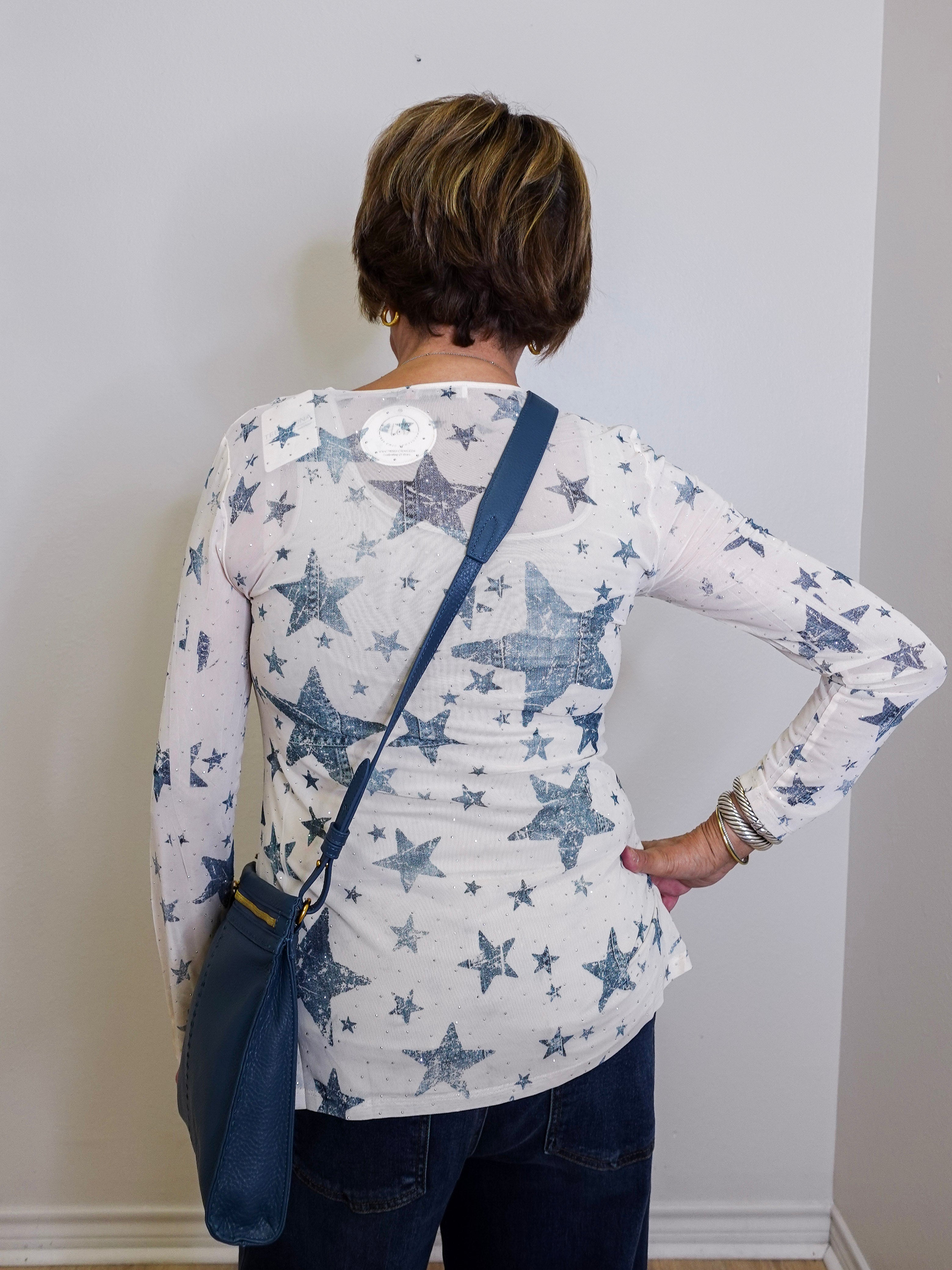 Person wearing a white long-sleeve shirt with blue star pattern, standing against a plain wall.