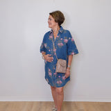 Woman wearing a blue floral dress with a beige bag against a white wall.