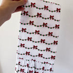 Hand holding a white fabric with red bow and green berry pattern against a plain background