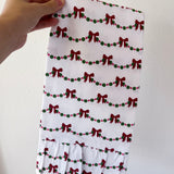 Hand holding a white fabric with red bow and green berry pattern against a plain background