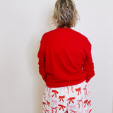 Person wearing a red sweatshirt and white shorts with red bows against a white wall