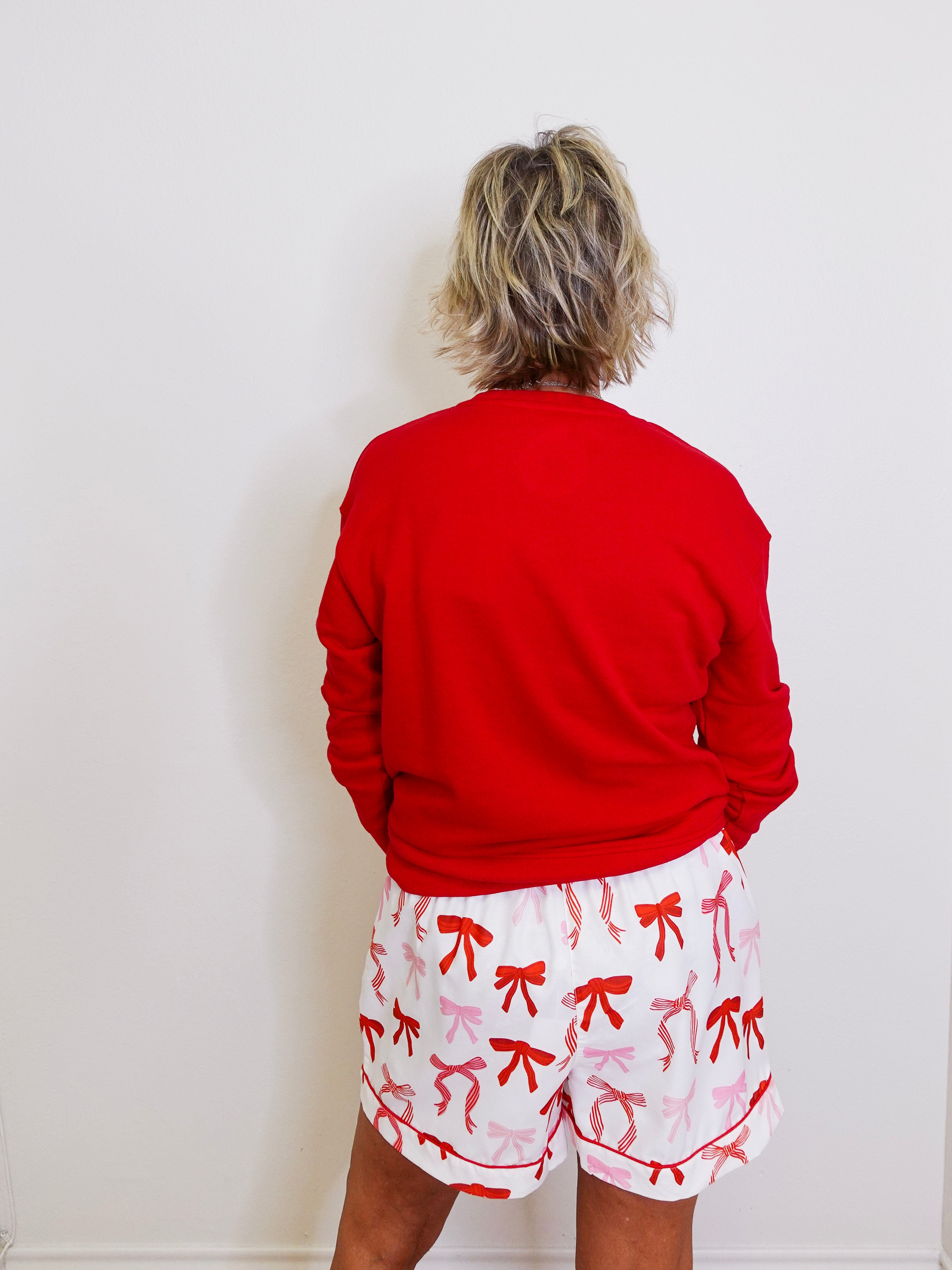 Person wearing a red sweatshirt and white shorts with red bows against a white wall