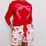 Person wearing a red sweater with a pink bow and white shorts with red bows on a plain background