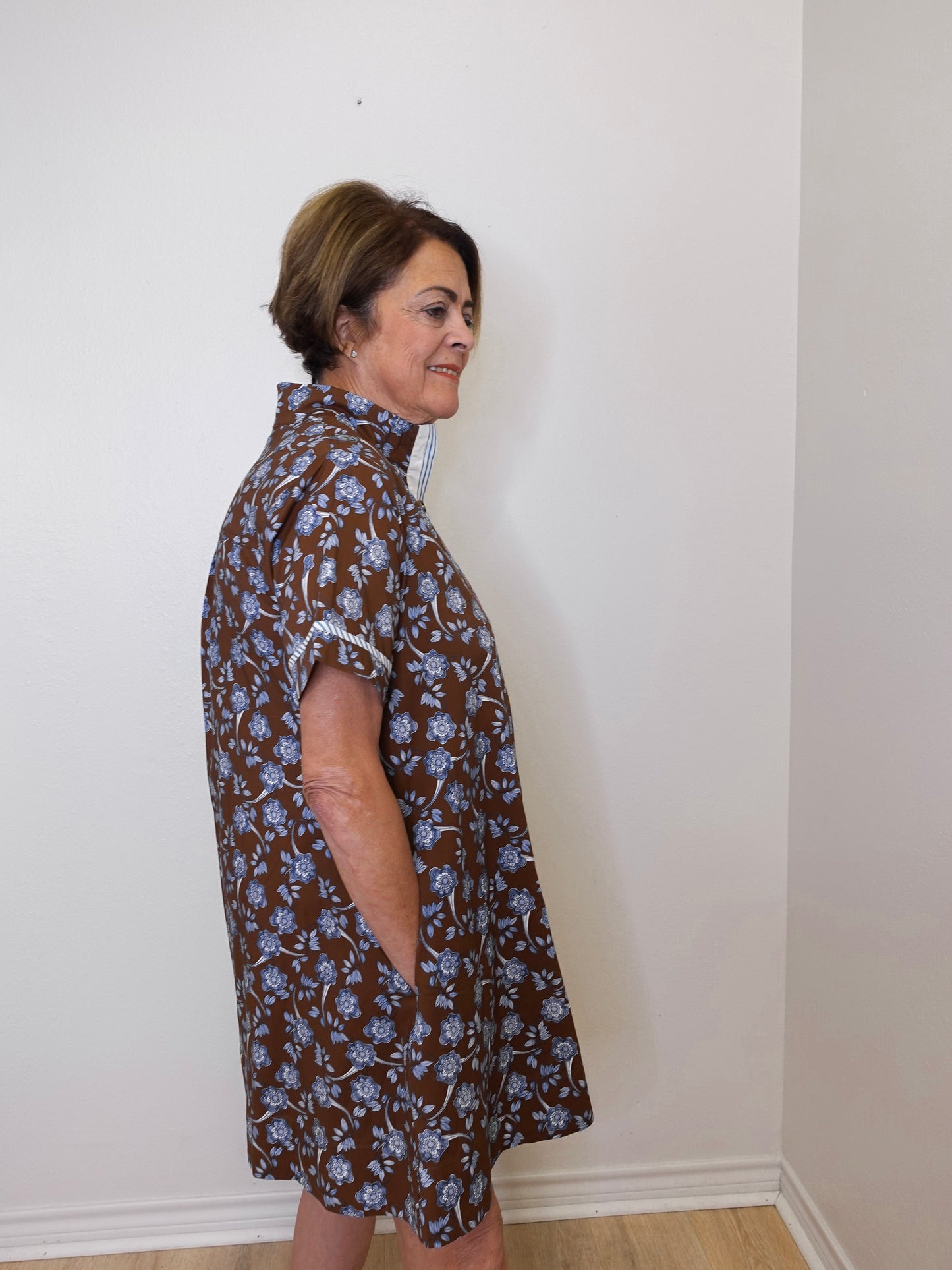 Woman wearing a brown floral dress against a white wall