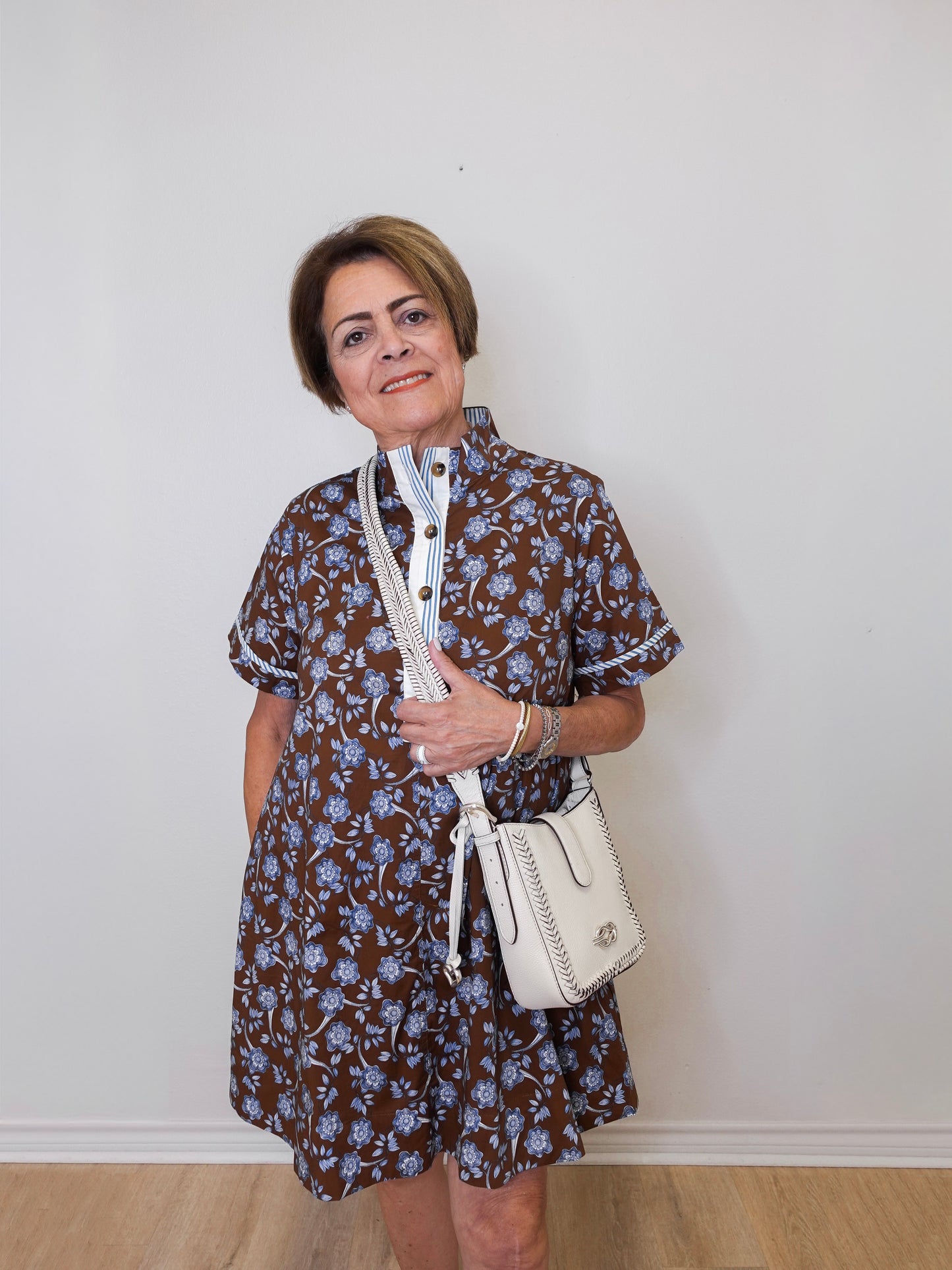Woman wearing a floral dress holding a white handbag against a plain background