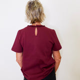 Person wearing a burgundy top with a cut-out back design against a white background