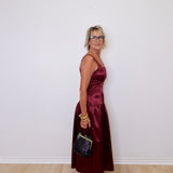 Woman in a burgundy dress holding a black handbag against a white wall.