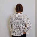 Person wearing a white crochet cardigan against a plain background