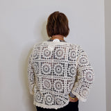 Person wearing a white crochet cardigan against a plain background