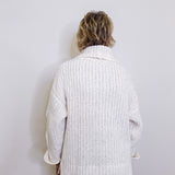 Person wearing a white knitted cardigan against a plain background