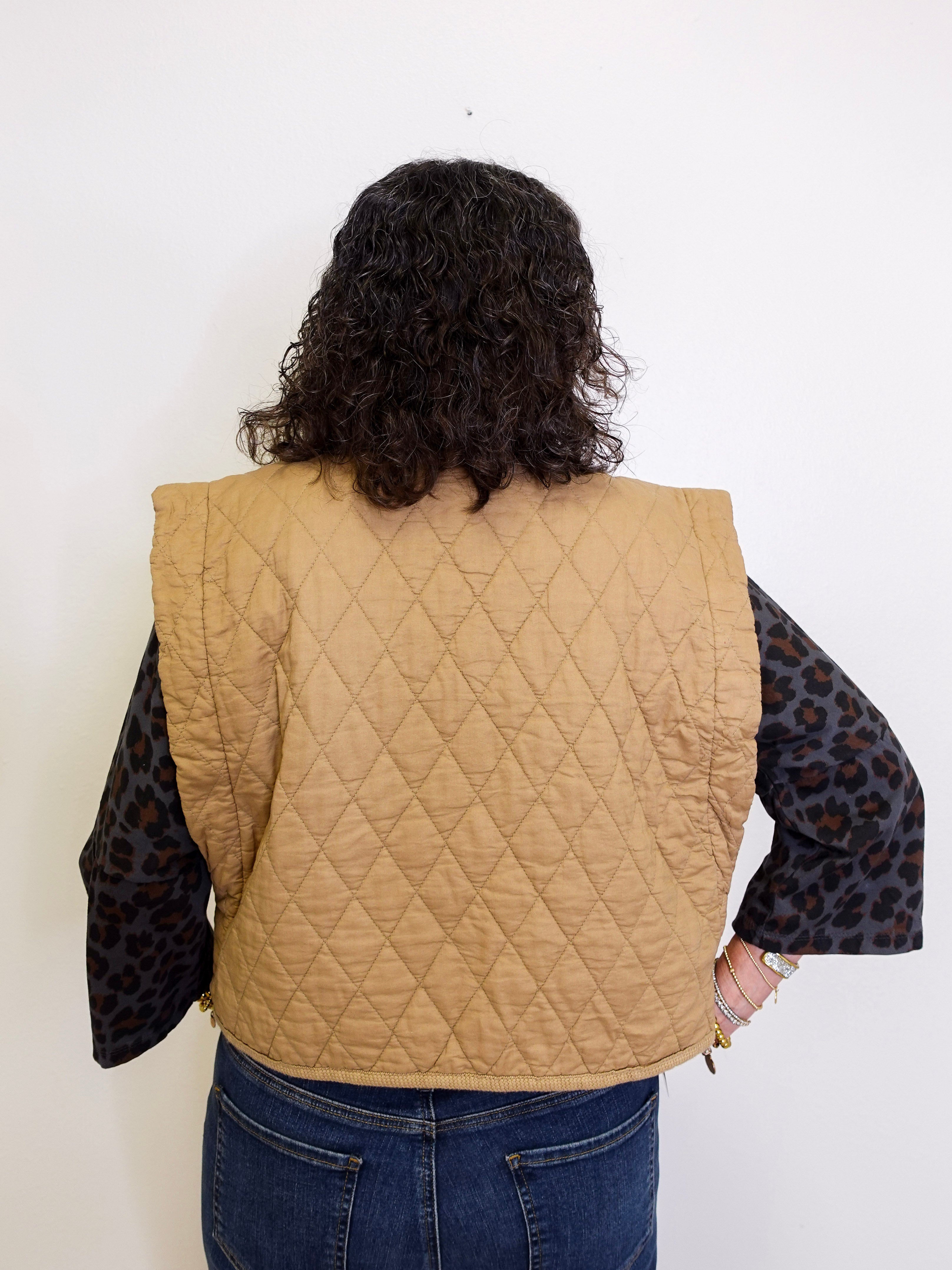 Person wearing a beige quilted vest with a white background
